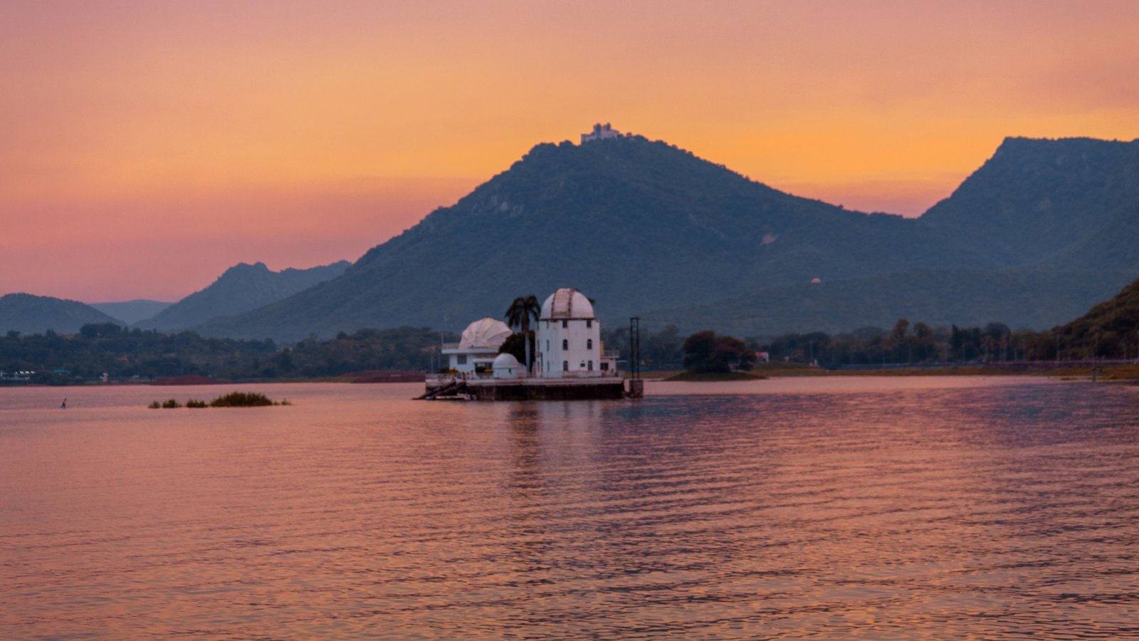 Fateh Sagar Lake in Udaipur, a tranquil blue expanse surrounded by Aravalli hills, with motorboats gliding across and Nehru Park island nestled at its heart.