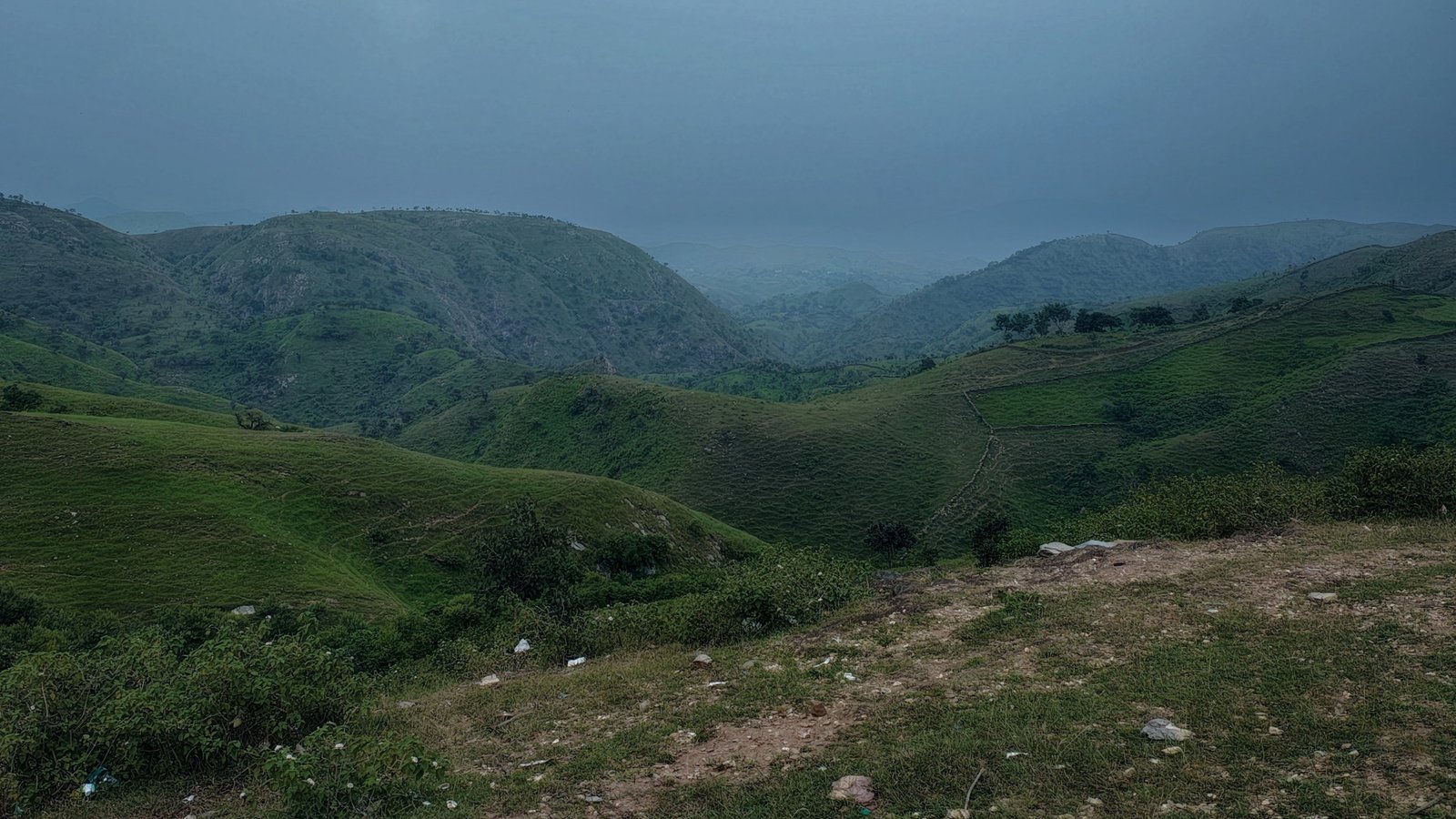 Panoramic view of Rayta Hills near Udaipur, with winding trails, lush monsoon greenery, and distant Aravalli silhouettes under a golden sky.